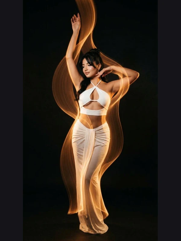 Woman in a flowing white outfit surrounded by amber light trails