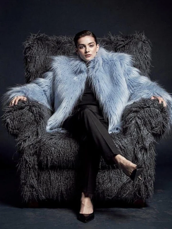 Woman in a pale blue winter coat seated in a dark armchair